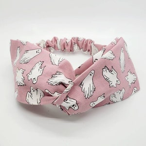 May include: A pink fabric headband with a white ghost pattern. The headband is twisted and tied in a knot.