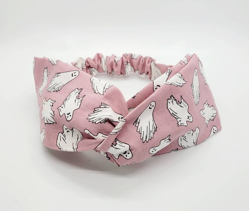 May include: A pink fabric headband with a white ghost pattern. The headband is twisted and tied in a knot.