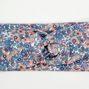 May include: A knotted headband with a floral pattern in shades of pink, blue, and green on a white background.
