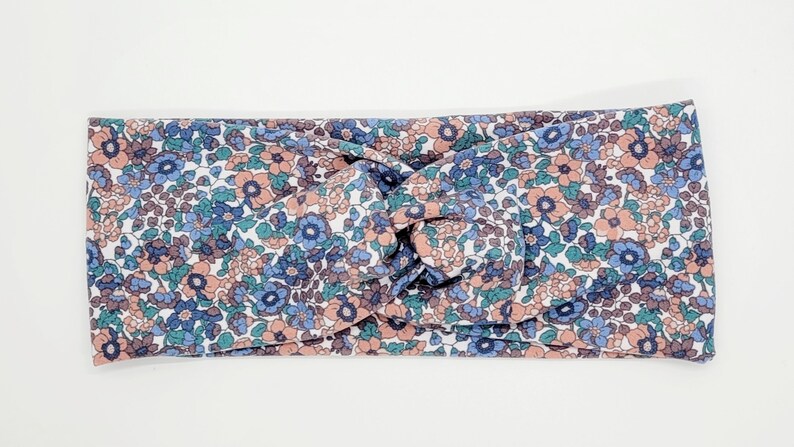 May include: A knotted headband with a floral pattern in shades of pink, blue, and green on a white background.
