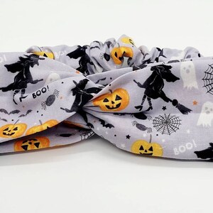 May include: A gray headband with a Halloween theme. The headband features a repeating pattern of orange pumpkins, black bats, black witches, white ghosts, and black spiderwebs. The text "BOO!" appears multiple times on the headband.