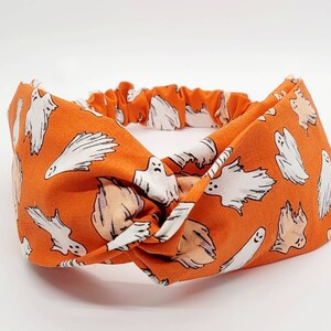 May include: Orange fabric headband with a white ghost pattern. The headband is knotted in the center.