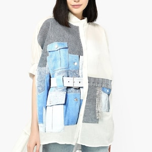 May include: A white, long-sleeved shirt with a patchwork design featuring denim, gray, and white fabric. The shirt has a white belt and a rhinestone detail on the pocket.