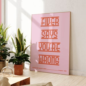 May include: A pink poster with the text "Fiver Says You're Wrong" in orange. The poster is framed in a thin wooden frame and is hanging on a white wall.