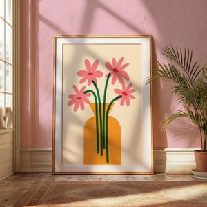 May include: A framed art print featuring a stylized floral arrangement. Pink flowers with green stems are in an orange vase against a cream background. The print is in a gold frame, set against a pink wall.