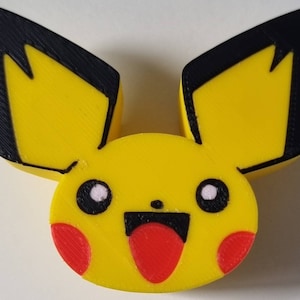 Könnte beinhalten: Eine gelbe 3D-gedruckte Figur von Pikachu, einem beliebten Pokémon-Charakter. Die Figur hat schwarze Ohren, rote Wangen und einen roten Mund.