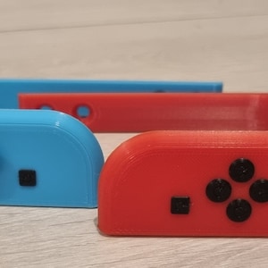 Könnte beinhalten: Zwei 3D-gedruckte Halter für Nintendo Switch Joy-Con-Controller. Einer ist blau und der andere rot.