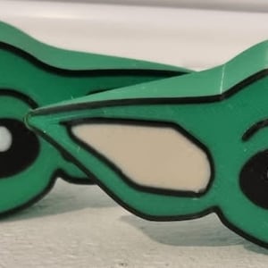 May include: Two green and white plastic figurines of a popular fictional character with large eyes and a mischievous expression. The figurines are approximately 7.5 cm tall.