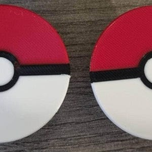 Puede incluir: Dos Pok&eacute; Balls rojas, blancas y negras. Las Pok&eacute; Balls son redondas y tienen una l&iacute;nea negra alrededor del medio. La mitad superior de las Pok&eacute; Balls es roja y la mitad inferior es blanca. Las Pok&eacute; Balls tienen un c&iacute;rculo negro con un centro blanco en el medio.