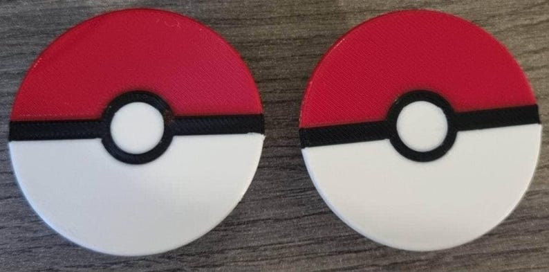 Puede incluir: Dos Pok&eacute; Balls rojas, blancas y negras. Las Pok&eacute; Balls son redondas y tienen una l&iacute;nea negra alrededor del medio. La mitad superior de las Pok&eacute; Balls es roja y la mitad inferior es blanca. Las Pok&eacute; Balls tienen un c&iacute;rculo negro con un centro blanco en el medio.