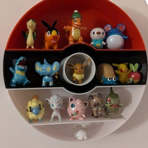 以下が含まれることがあります： 白、赤、黒のポケボール型の棚に、小さなポケモンのフィギュアが13体並んでいます。フィギュアは3段の棚に並んでいます。上の棚には6体、真ん中の棚には5体、下の棚には2体のフィギュアが並んでいます。