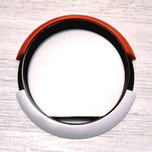 Può includere: Un oggetto circolare multicolore con un centro bianco. La sezione superiore è di un rosso vibrante, che sfuma nel nero, con una parte inferiore grigio argento. L'oggetto è probabilmente un elemento decorativo o parte di un design più ampio.