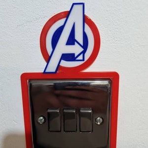 May include: A red and white light switch cover with a 3D printed Avengers logo featuring a white "A" with a blue circle and red outer ring.