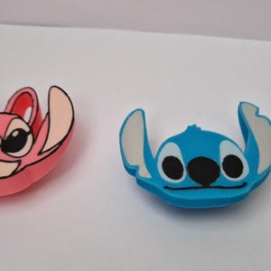 Op de afbeelding: Twee Stitch-figuurtjes, een roze en een blauwe. De roze Stitch heeft grote zwarte ogen en een roze lichaam. De blauwe Stitch heeft grote zwarte ogen en een blauw lichaam.