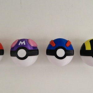 Pode incluir: Cinco Poké Balls de diferentes cores com desenhos em preto e branco. As Poké Balls são vermelha, roxa, azul, amarela e preta.