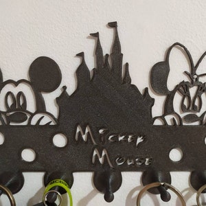 May include: Black metal key holder with Mickey Mouse and Minnie Mouse silhouettes, a silhouette of Cinderella's castle, and the text "Mickey Mouse". The key holder has six hooks.