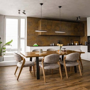 May include: A wooden dining table with six chairs. The table has a light wood finish and the chairs are upholstered in a light gray fabric. The table is set with placemats and napkins. The room has a modern design with white walls and a brown backsplash.