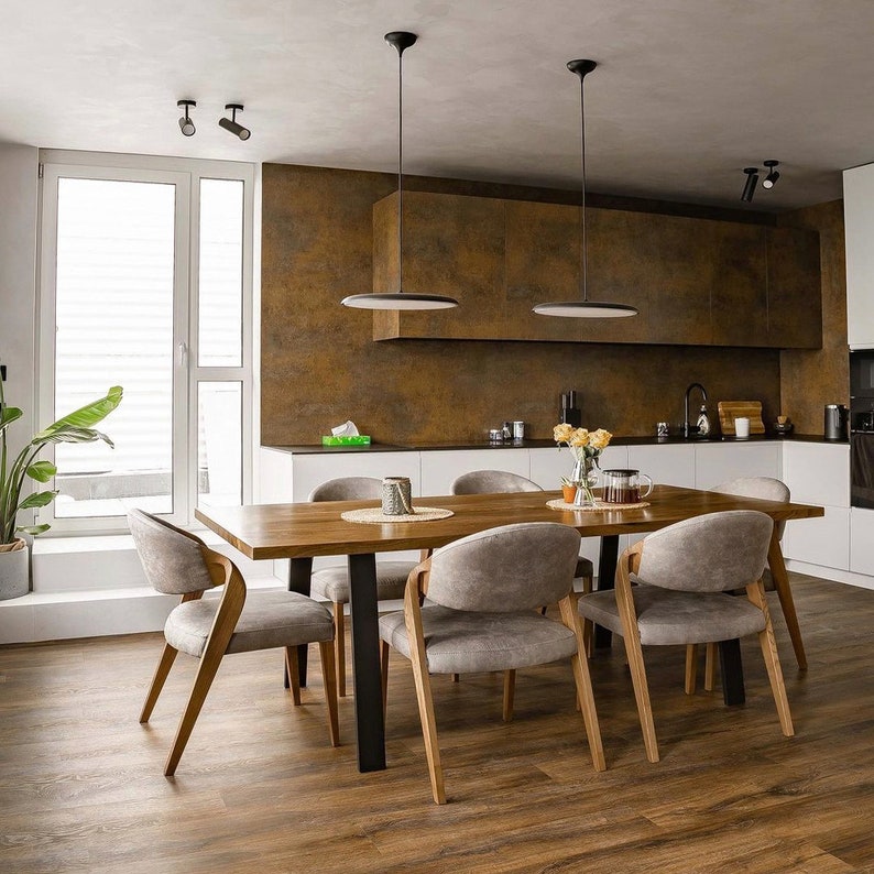 May include: A wooden dining table with six chairs. The table has a light wood finish and the chairs are upholstered in a light gray fabric. The table is set with placemats and napkins. The room has a modern design with white walls and a brown backsplash.