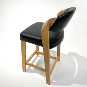 May include: A black leather chair with a wooden frame and a curved back. The chair has a square base with a wooden support structure.