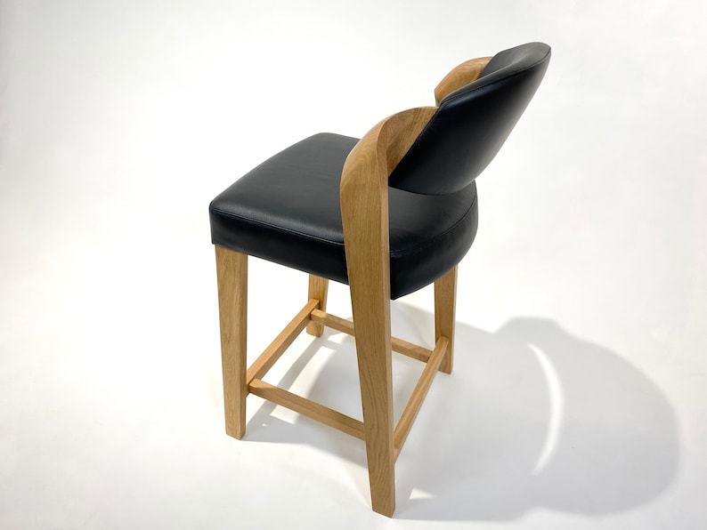 May include: A black leather chair with a wooden frame and a curved back. The chair has a square base with a wooden support structure.