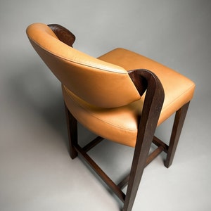 May include: A brown wooden chair with a tan leather seat and back. The chair has a unique design with curved arms and a slightly rounded back.