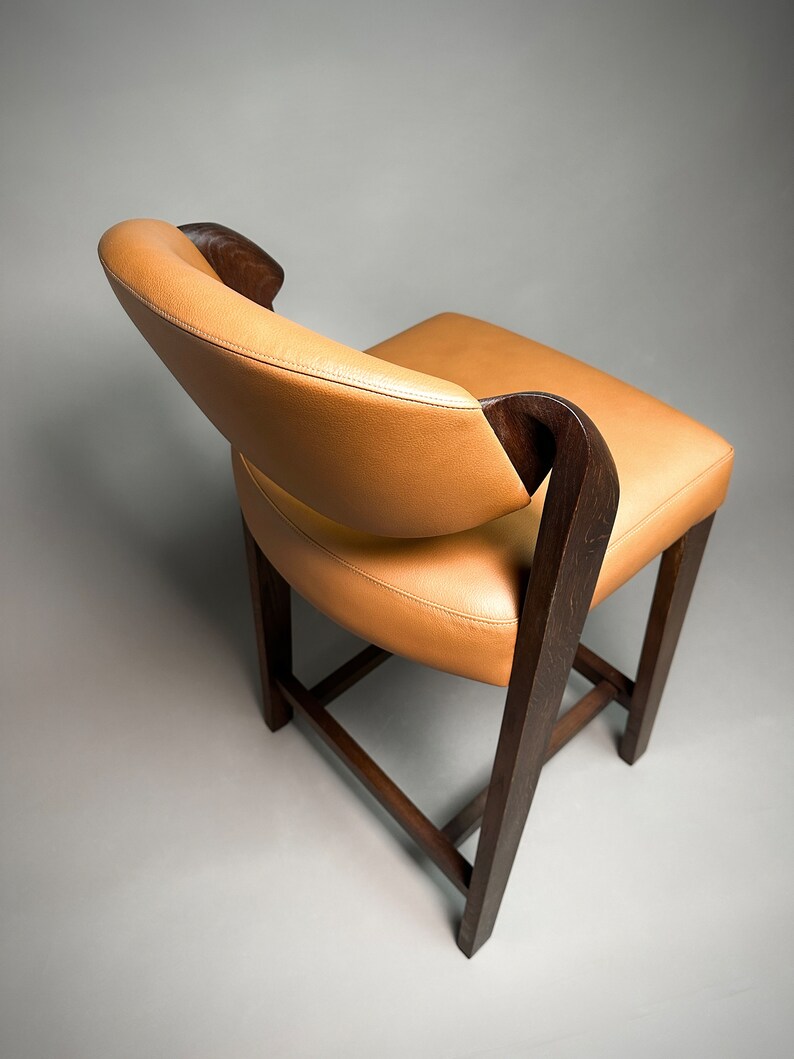 May include: A brown wooden chair with a tan leather seat and back. The chair has a unique design with curved arms and a slightly rounded back.