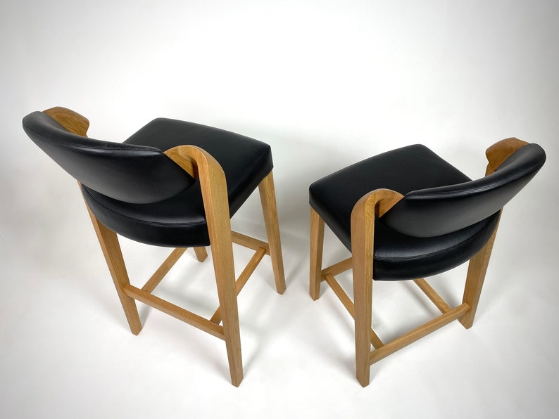 May include: Two black leather bar stools with wooden frames. The stools have a curved back and a simple design.