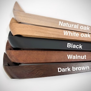 K&ouml;nnte beinhalten: Nahaufnahme von f&uuml;nf Holzregalen in verschiedenen Farben: Natureiche, Wei&szlig;eiche, Schwarz, Walnuss und Dunkelbraun. Jedes Regal hat ein gebogenes Design und der Farbname ist wei&szlig; aufgedruckt.