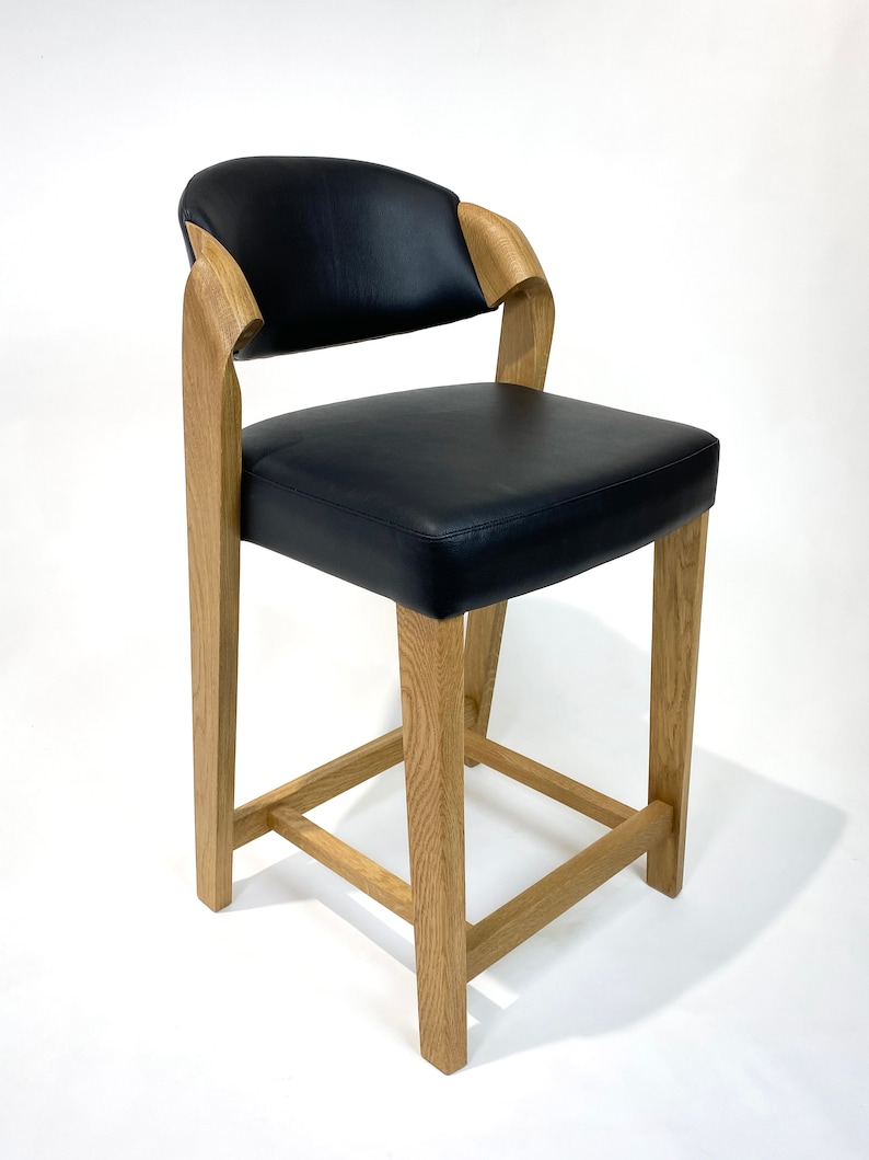 May include: A black leather bar stool with a curved back and wooden legs. The stool has a simple, modern design.
