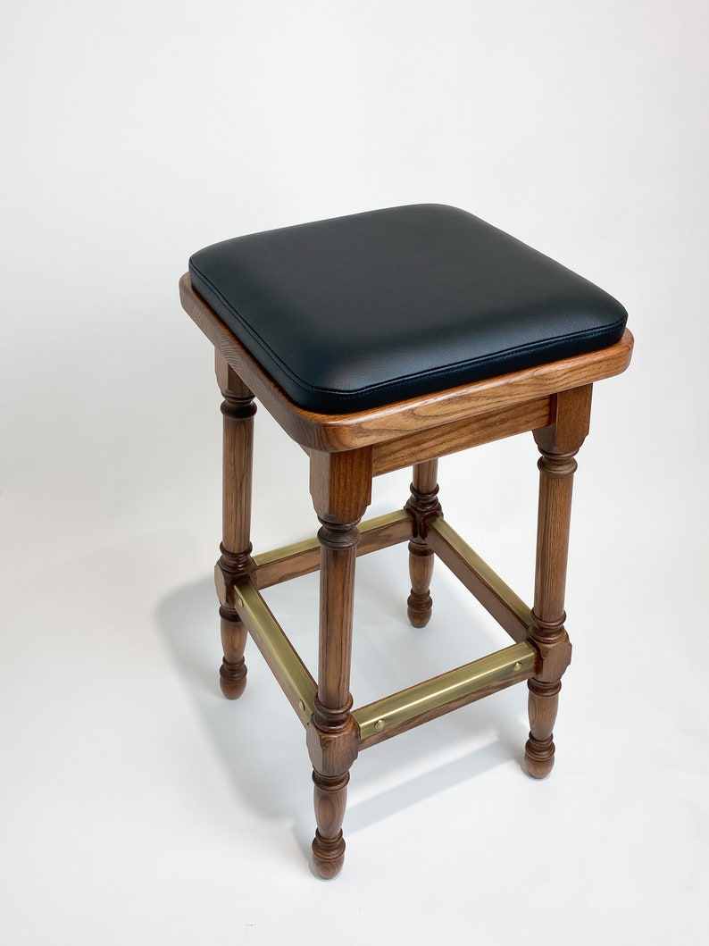 May include: A wooden bar stool with a black leather seat and brass accents. The stool has a square base and turned legs.