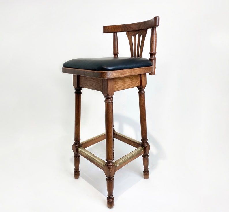May include: A wooden bar stool with a black leather seat and a brass footrest. The stool has a traditional design with a curved back and turned legs.