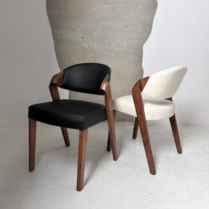 May include: Two chairs with wooden frames and upholstered seats. One chair has a black leather seat and the other has a white leather seat.