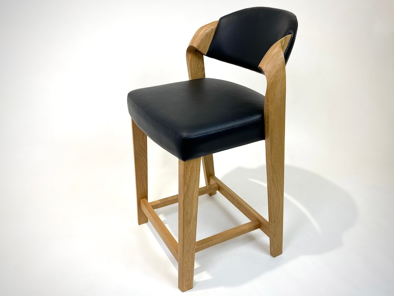 May include: A black leather upholstered counter stool with a wooden frame. The stool has a curved back and a square base.