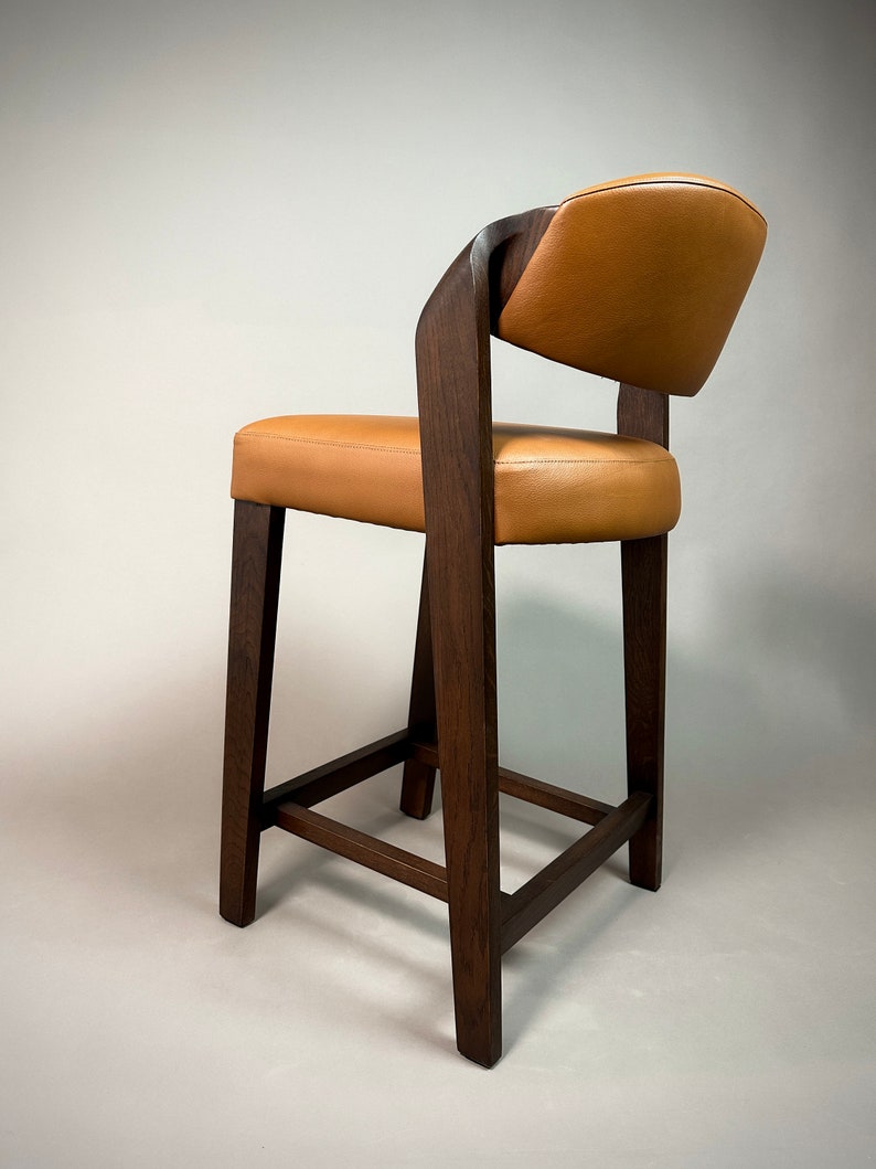May include: A brown wooden bar stool with a tan leather seat and back. The stool has a simple, modern design with a square base and a curved back.