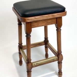 May include: A wooden bar stool with a black leather seat and brass accents. The stool has a square seat and four turned legs.
