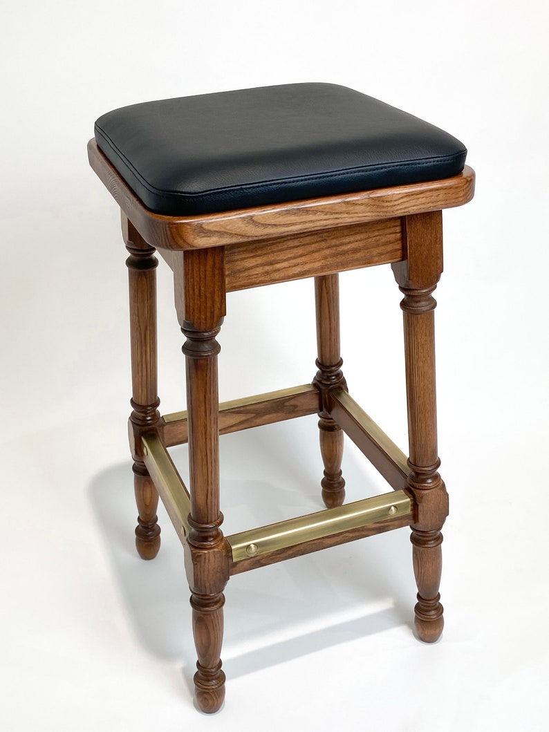 May include: A wooden bar stool with a black leather seat and brass accents. The stool has a square seat and four turned legs.