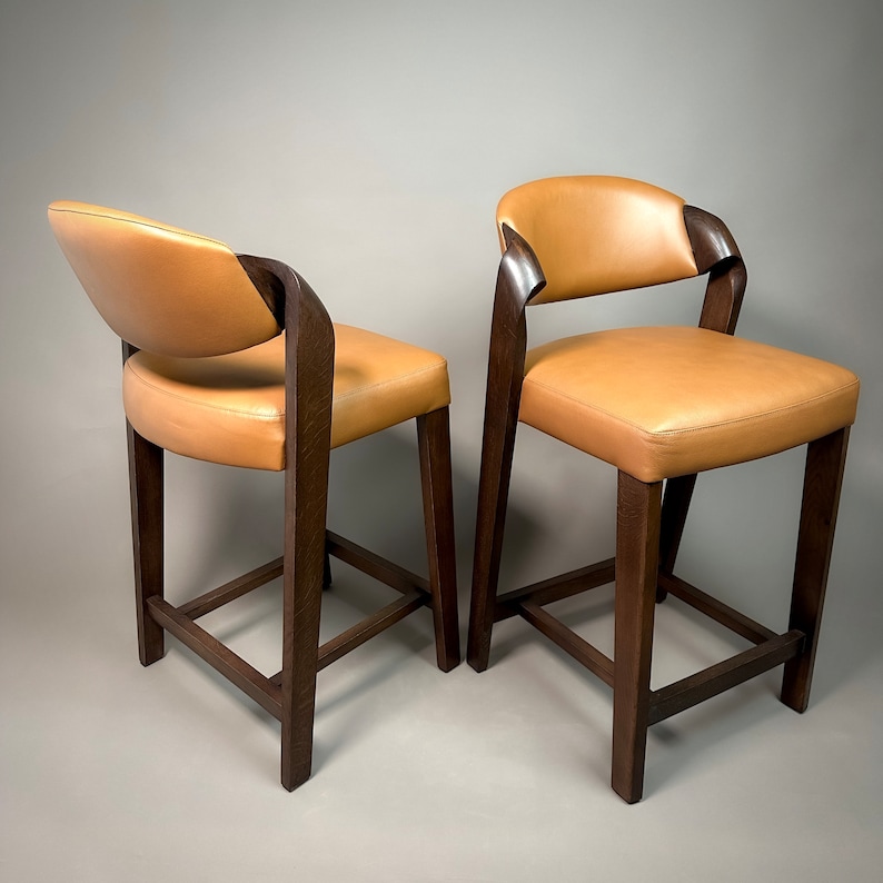 May include: Two brown wooden bar stools with tan leather seats. The stools have a simple, modern design.