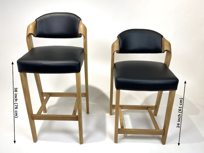 May include: Two black leather bar stools with wooden frames. The taller stool is 30 inches (76 cm) high and the shorter stool is 24 inches (61 cm) high.