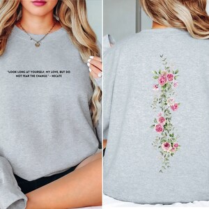 K&ouml;nnte beinhalten: Grauer Pullover mit einem Zitat auf der Vorderseite und einem Blumendesign auf der R&uuml;ckseite. Das Zitat lautet "Schau lange auf dich selbst, meine Liebe, aber f&uuml;rchte dich nicht vor dem Wandel - Hekate".