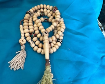 May include: A white bone mala prayer beads with turquoise, red, and gold accents. The mala has a long tassel with a green and white fringe.