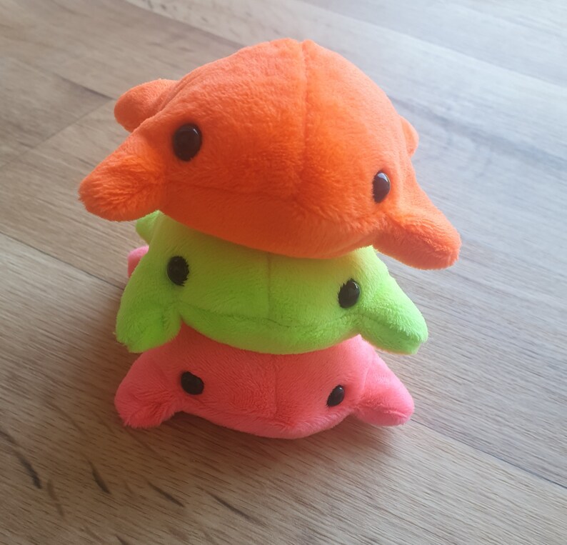 May include: A stack of three plush toys in the shape of a fish. The top toy is orange, the middle toy is green, and the bottom toy is pink.