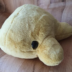 May include: A plush yellow dolphin toy with black eyes. The dolphin is lying on its side with its head turned to the right.
