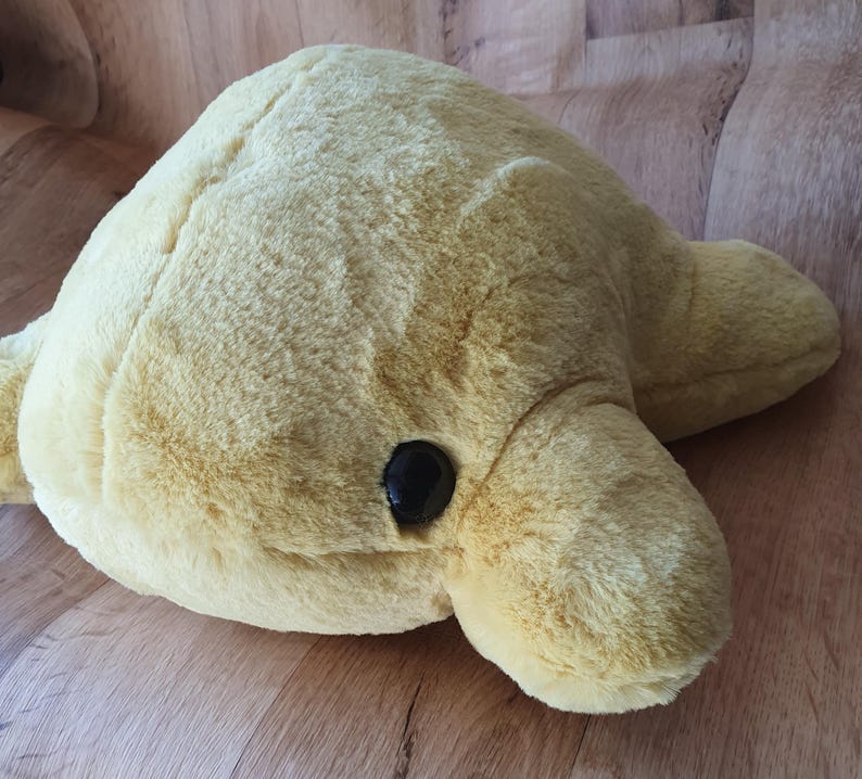 May include: A plush yellow dolphin toy with black eyes. The dolphin is lying on its side with its head turned to the right.
