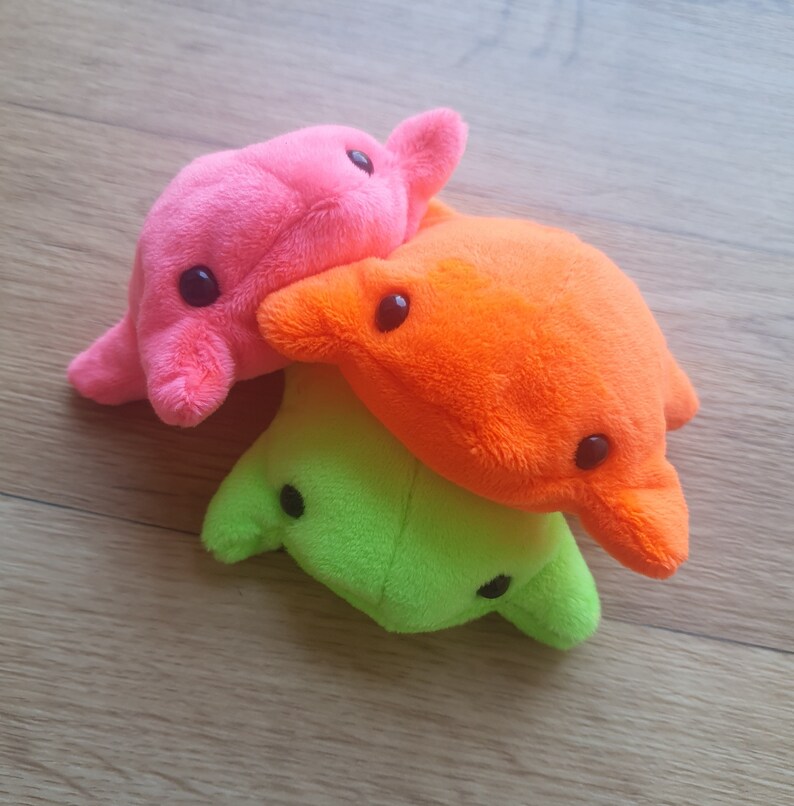 May include: Three plush toys stacked on top of each other. The top toy is pink, the middle toy is orange, and the bottom toy is green.