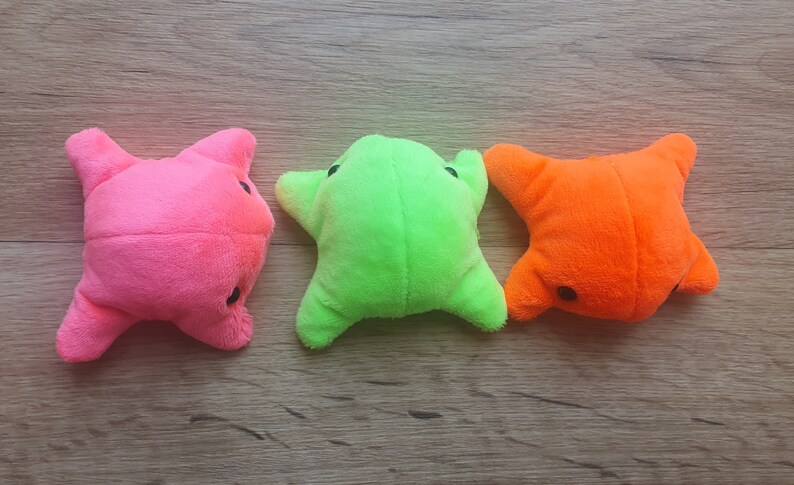 May include: Three plush toys shaped like stars in pink, green, and orange. The toys are lying on a wooden surface.