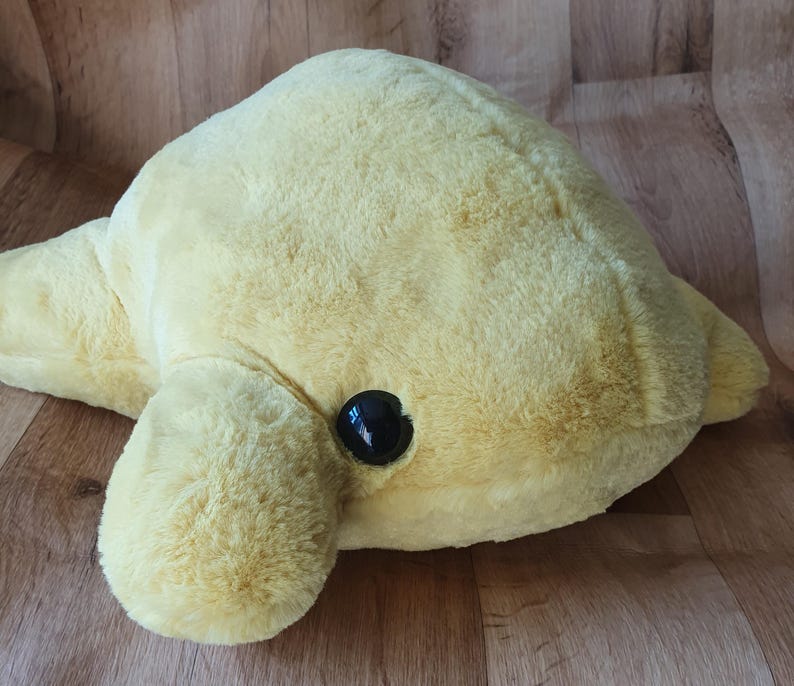 May include: A plush yellow dolphin toy with a black eye. The dolphin is lying on its side with its head turned to the left.