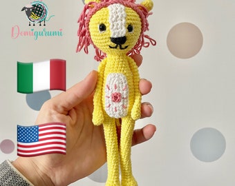 May include: A crocheted yellow lion with a pink mane and white face. The lion has a pink flower on its chest and is holding a small white flower.