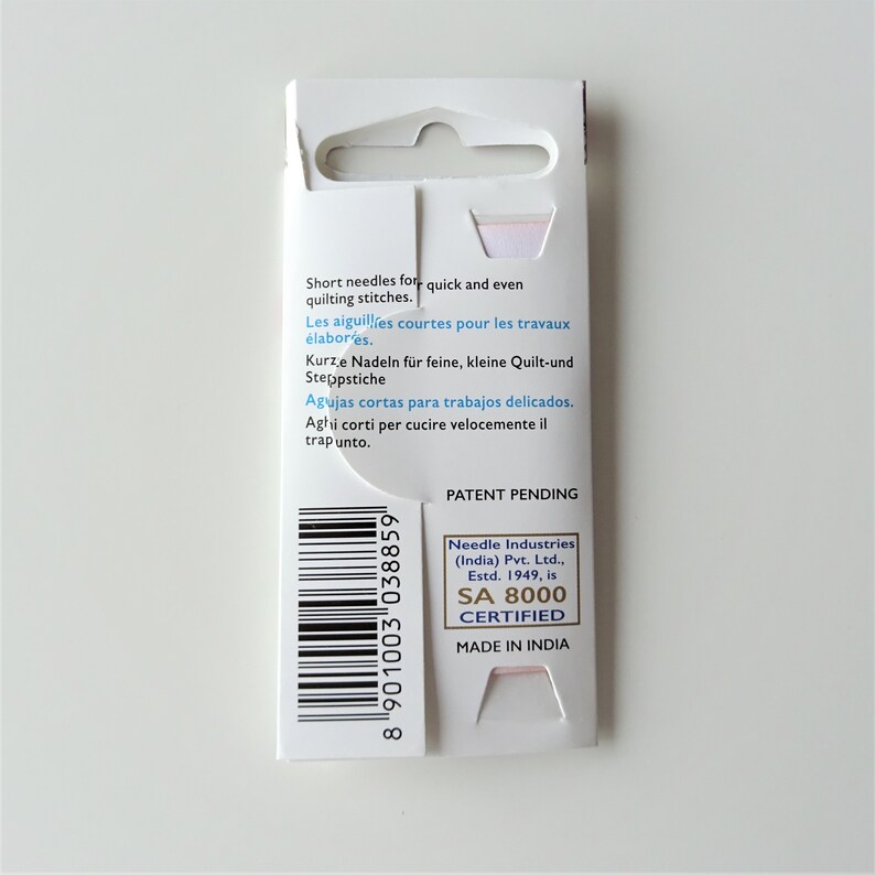 May include: A white cardboard package with a barcode and text in multiple languages. The text reads "Short needles for quick and even quilting stitches."  "Les aiguilles courtes pour les travaux elabores." "Kurze Nadeln fur feine, kleine Quilt-und Steppstiche" "Agujas cortas para trabajos delicados." "Aghi corti per cucire velocemente il trapunto."  "Patent Pending" "Needle Industries (India) Pvt. Ltd., Estd. 1949, is SA 8000 CERTIFIED MADE IN INDIA"