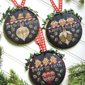 May include: Three round Christmas baubles with a dark blue background and gold trim. Each bauble features a different festive message: "Joy to the World", "Happy Holidays", and "Peace on Earth".