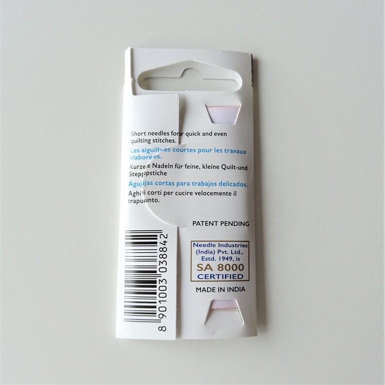 May include: A white cardboard package with a barcode and text that reads "Short needles for quick and even quilting stitches."  The package also includes the text "Patent Pending" and "Needle Industries (India) Pvt. Ltd., Estd. 1949, is SA 8000 CERTIFIED MADE IN INDIA".